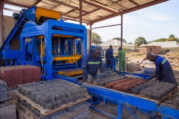 A QT6-15 block machine with color feeder producing interlocking pavers at a Tanzanian affordable housing construction site